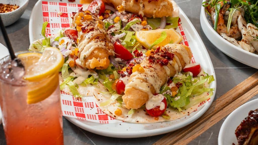 Battered fish tacos with lemon, tomato and slaw next to a pink drink, a casual bistro favourite at Bistro 1925