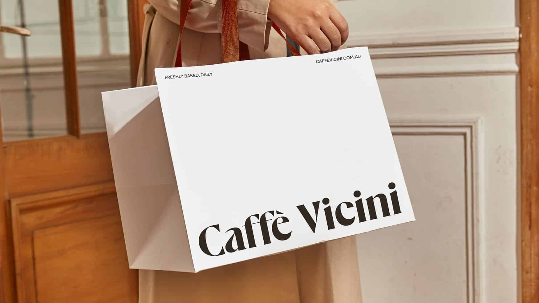 Customer holding Caffe Vicini takeaway bag reading Freshly baked daily outside the café entrance