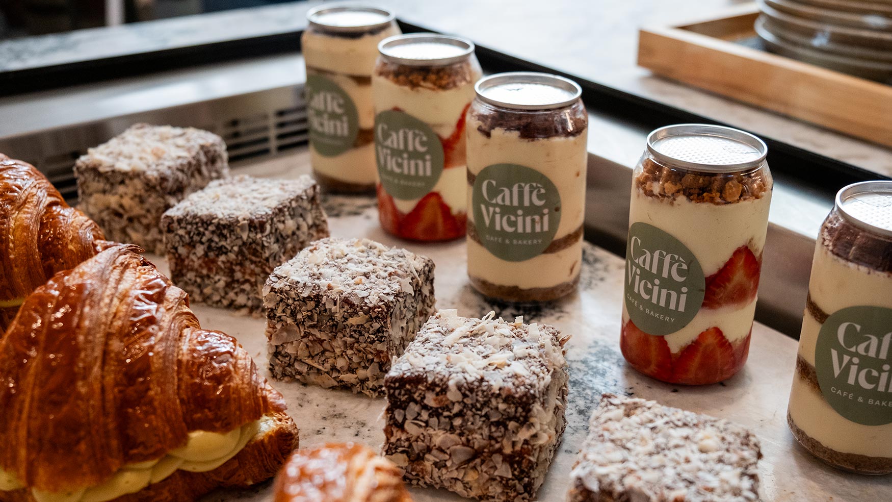 Assorted Caffe Vicini desserts including lamingtons, croissants, and layered jar cakes displayed on a café counter