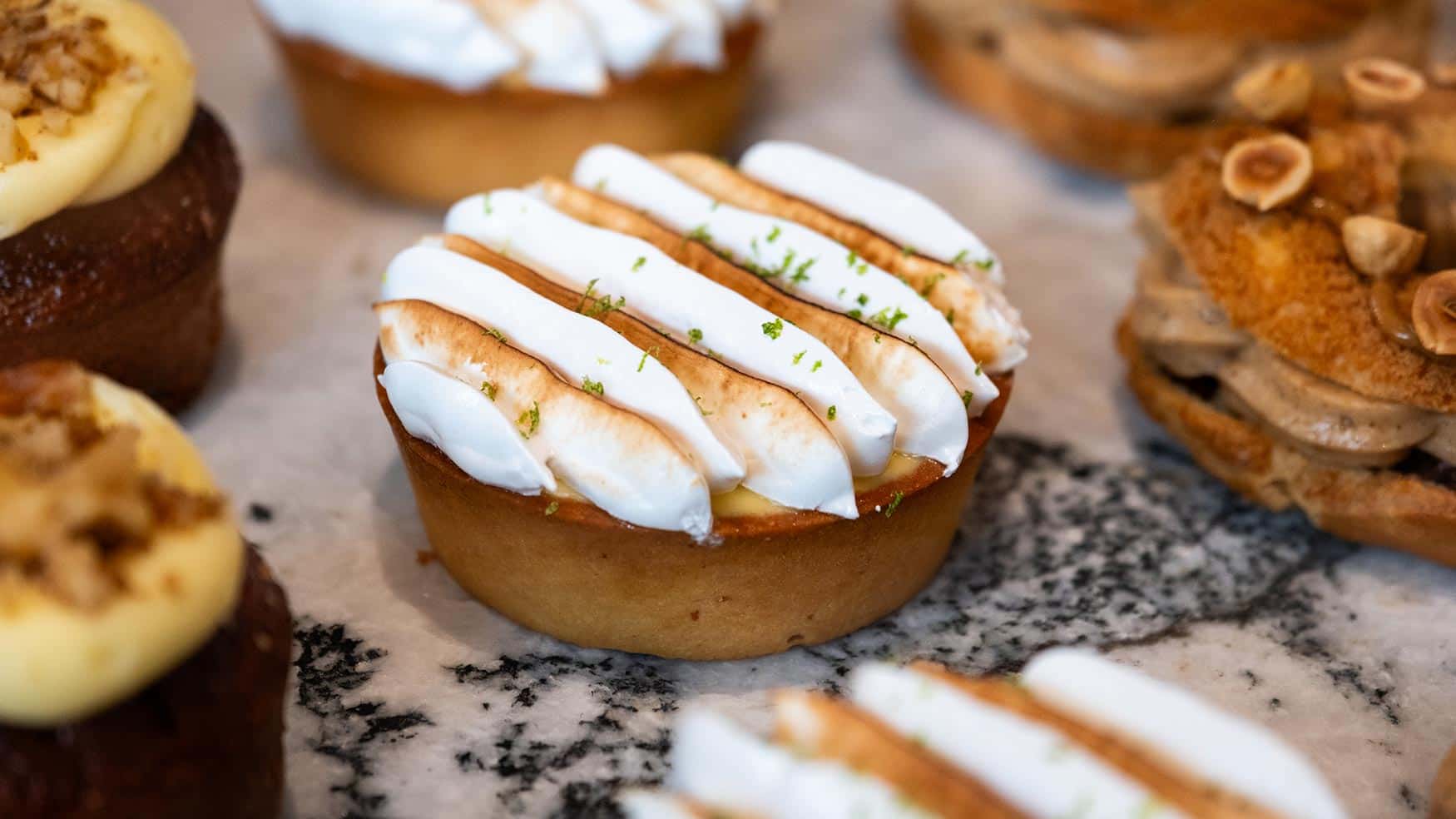 Lemon tart topped with toasted meringue and lime zest, displayed among assorted pastries at Caffe Vicini bakery counter