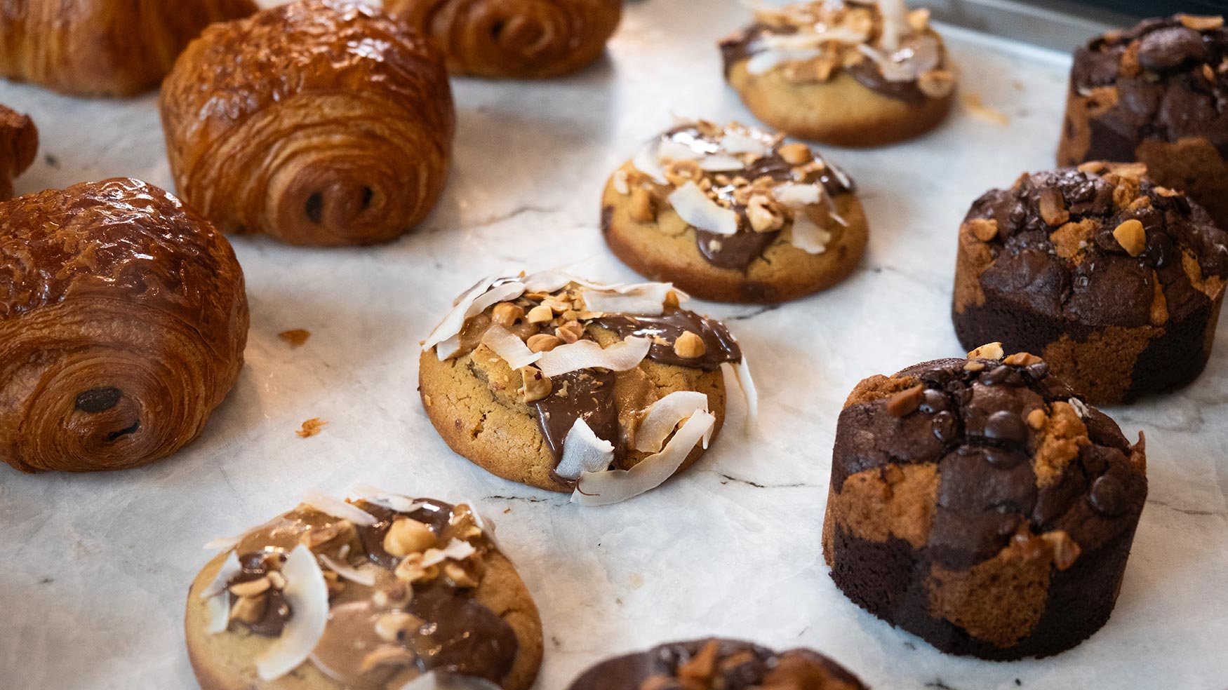Assorted pastries at Caffe Vicini including golden croissants, chocolate muffins, and nut-topped cookies on marble counter