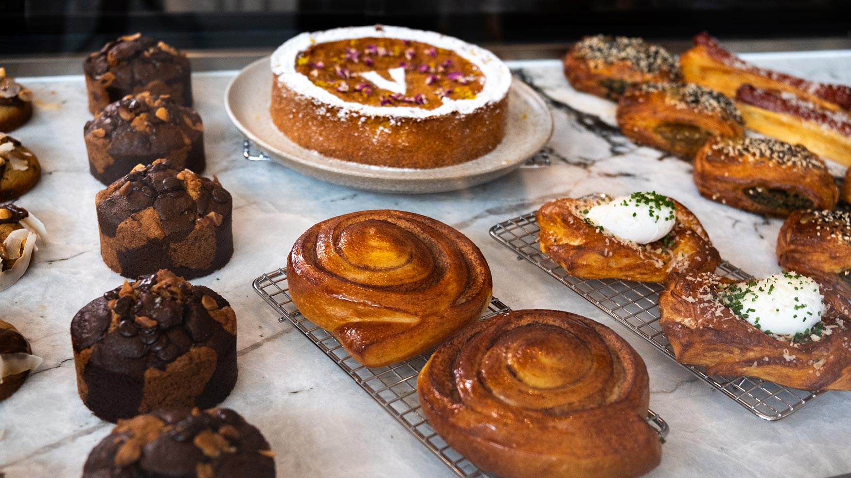 Freshly baked pastries at Caffe Vicini, including cinnamon scrolls, muffins, cakes and savoury danishes on marble counter