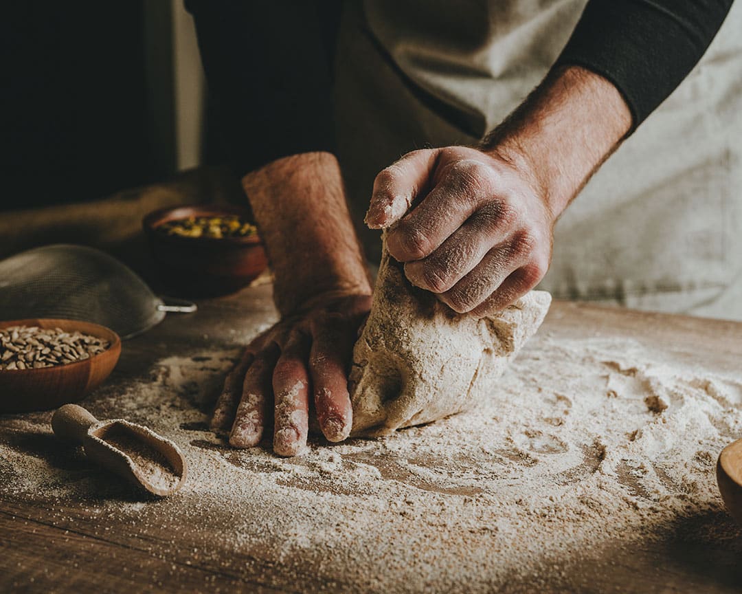 Baker’s hands kneading fresh dough on a floured wooden bench, capturing the artisanal baking process at Caffè Vicini.