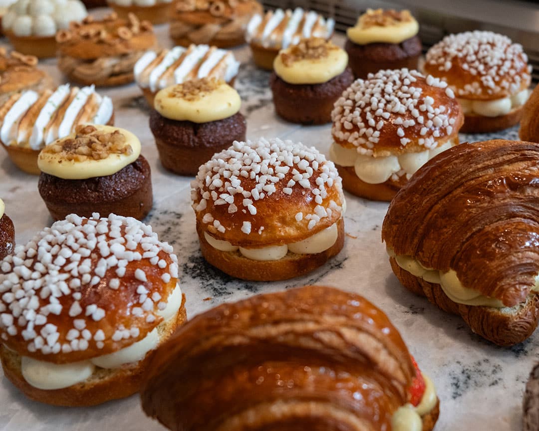 Assorted Caffè Vicini pastries including cream-filled brioche, croissants, and iced cakes neatly arranged on a marble counter.