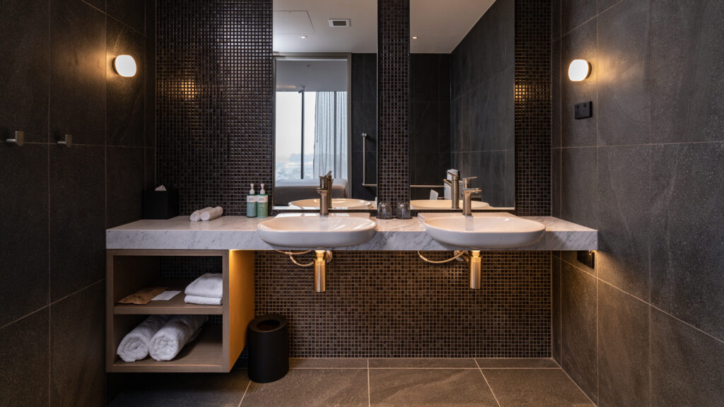 Twin basins on a marble vanity with dark tiles in the Superior Accessible King bathroom at Novotel Sydney Cabramatta