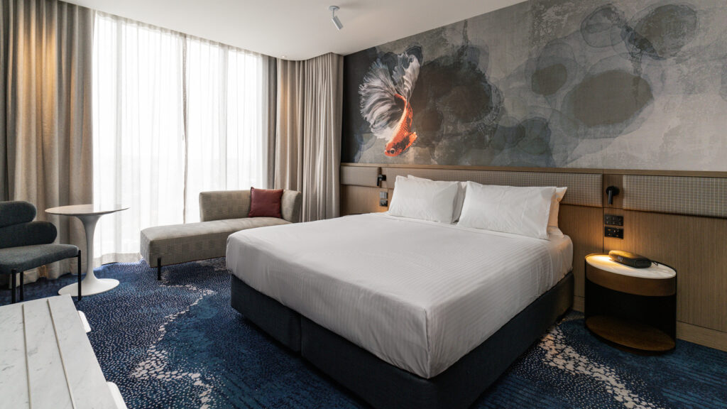 King bedroom in the Presidential Suite at Novotel Sydney Cabramatta with plush bed, lounge seating, and fish mural.