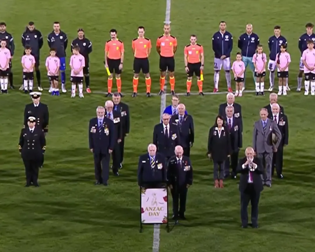 ANZAC Day ceremony on a football field with veterans, officials, and MCARTHUR BULLS FC MEMBERS standing in tribute