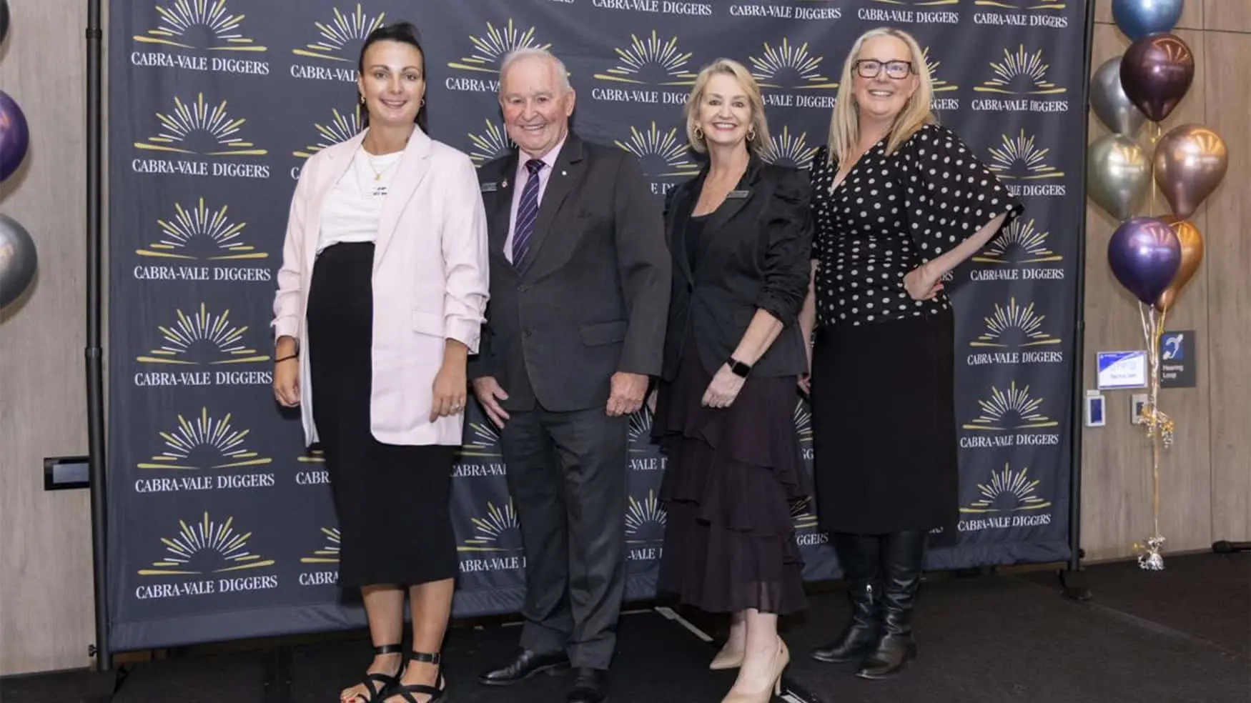 Guests posing for a photo at the Cabravale Club Resort ClubGRANTS Presentation, standing in front of a Cabravale Diggers branded backdrop.
