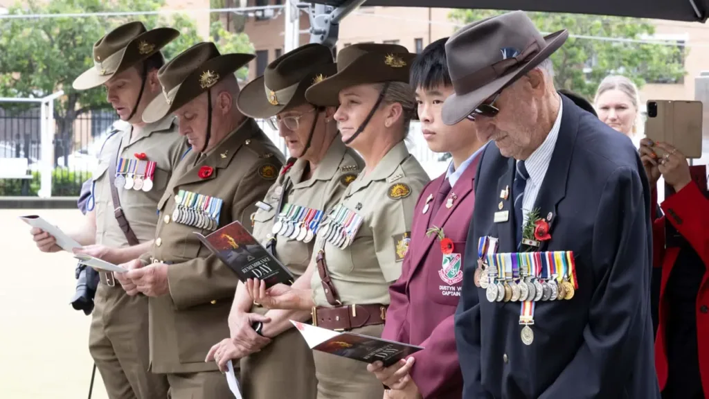 Veterans wearing medals bow heads during Remembrance Day ceremony at Cabravale Club Resort, honouring service and sacrifice