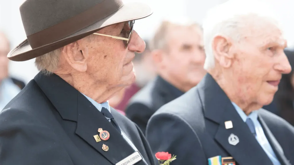 Elderly veterans wearing medals attend a Remembrance Day service, reflecting quietly during the ceremony