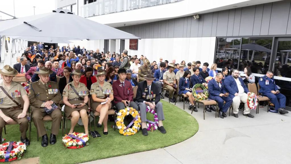 Veterans, service personnel and community members seated with wreaths at the ANZAC Day service at Cabravale