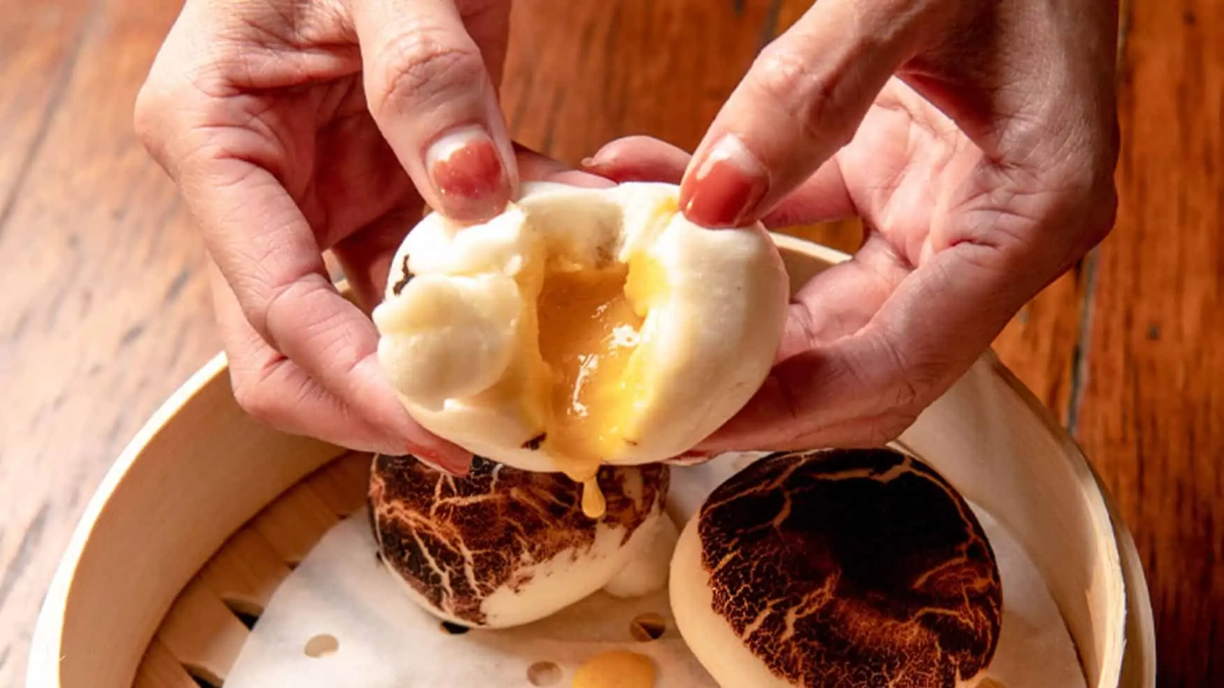 Steamed bao bun with rich savoury filling being pulled apart on bamboo steamer at District 8 Asian dining.