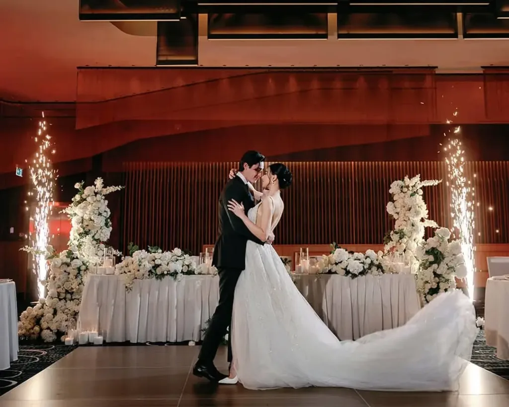 Bride and groom share a kiss on the dance floor, framed by white florals and sparklers at a Cabravale wedding