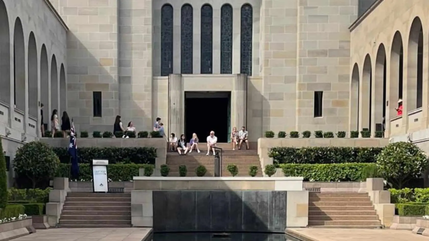 Visitors sit quietly at the Australian War Memorial courtyard before the Last Post Ceremony, reflecting in a solemn setting