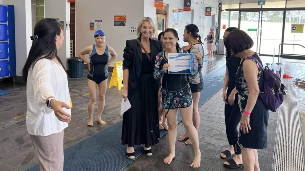 Learn to Swim participant holding a certificate beside a Cabravale representative on a Fairfield pool deck
