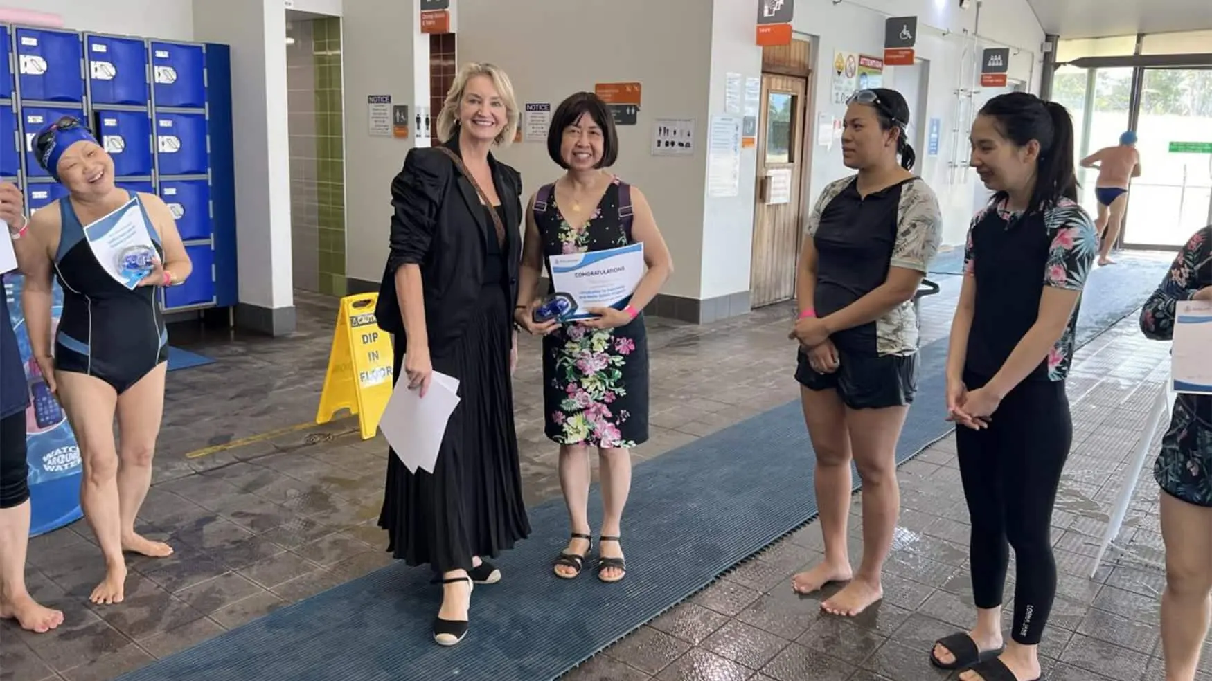 Learn to Swim participant receives a certificate alongside organisers and fellow swimmers at a Fairfield leisure centre.