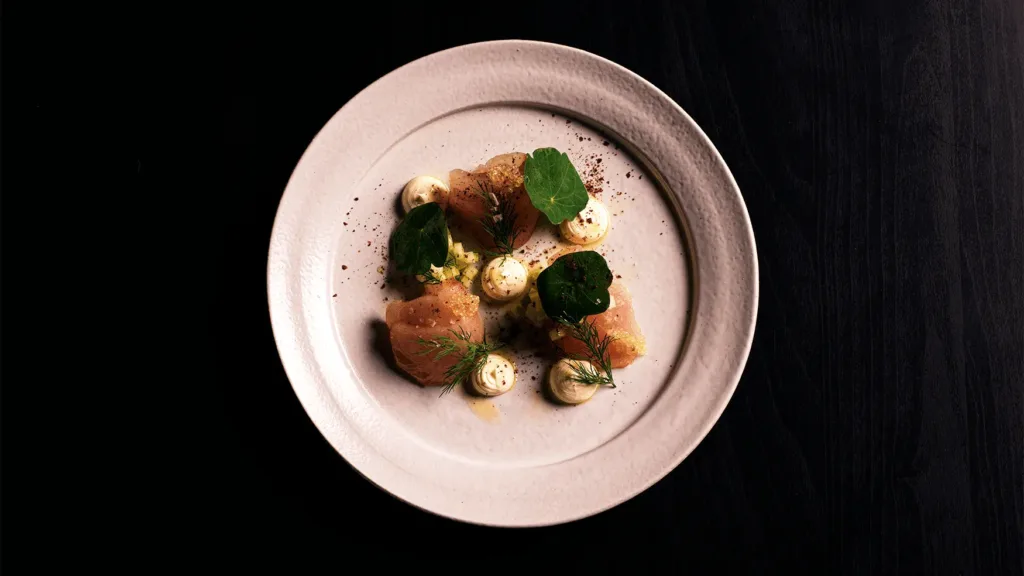 Finely plated fish dish with herb garnish and piped sauce at Magma by Dany Karam