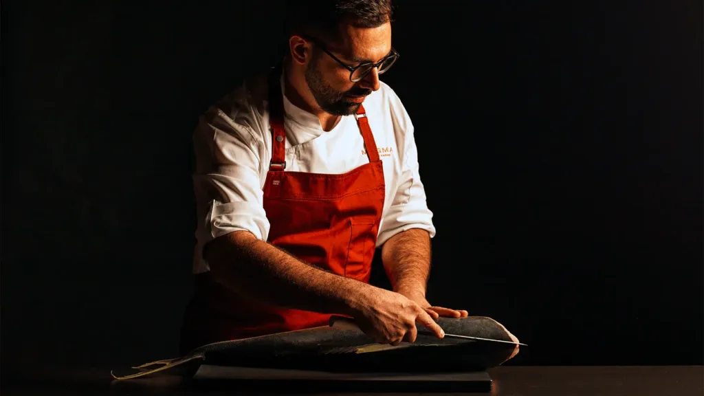 Chef carefully slicing a whole fish during preparation at Magma by Dany Karam