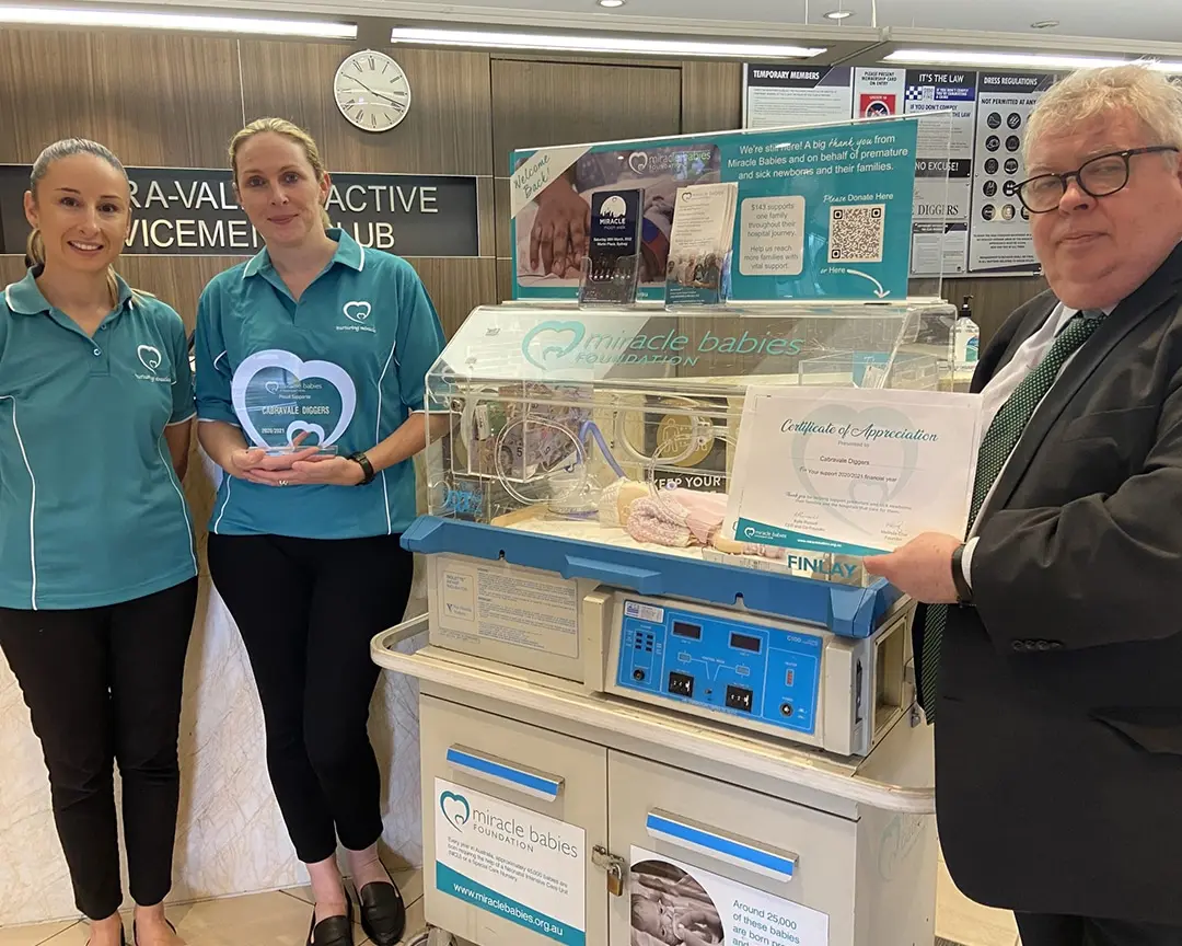 Cabravale Club Resort representatives and Miracle Babies Foundation staff standing beside a neonatal crib fundraising display, with a certificate of appreciation presented in support of premature and sick newborns.