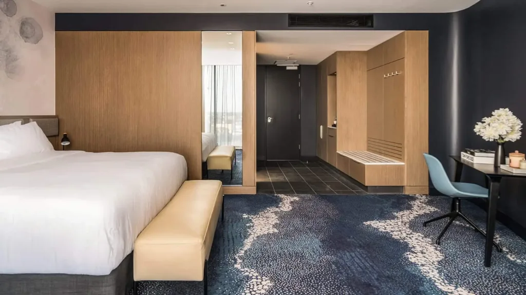 Superior King room with plush bed, workspace, mirrored wardrobe, bench seating and entry hall at Novotel Sydney Cabramatta