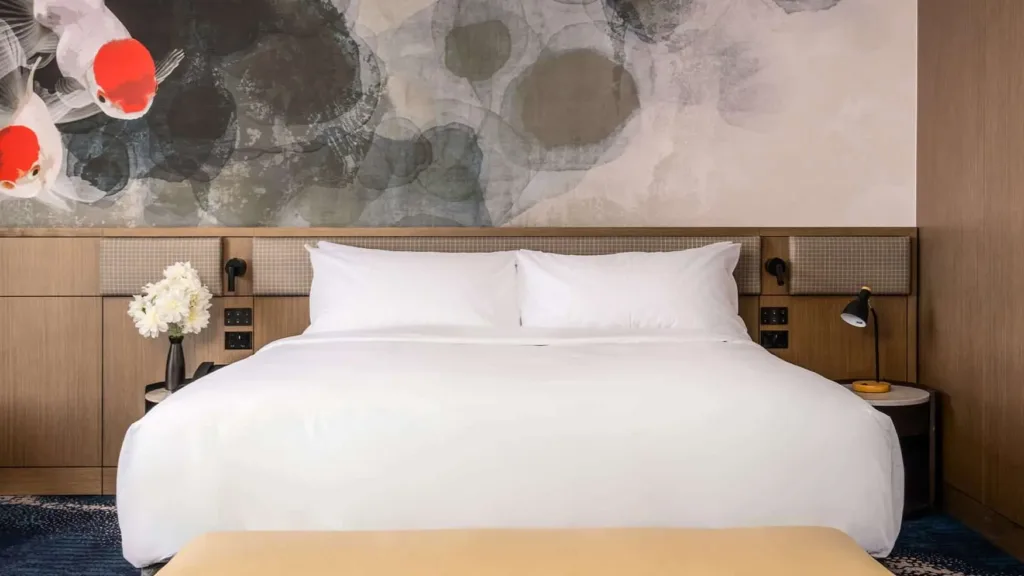 King bed with bedside lamps and white flowers beneath a koi fish mural in the Superior King room at Novotel Sydney Cabramatta