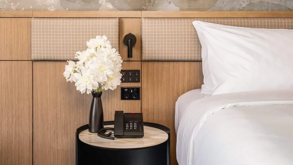 Bedside table with white flowers and a phone next to the king bed in the Superior King room at Novotel Sydney Cabramatta