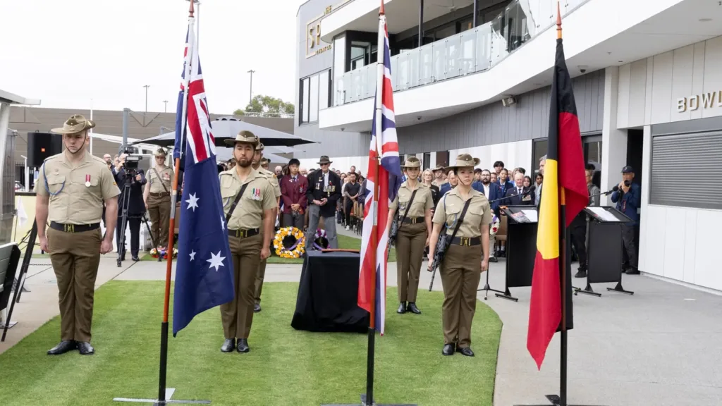 Army personnel at attention beside the Australian, British and Aboriginal flags at Remembrance Day 2024 at Cabravale