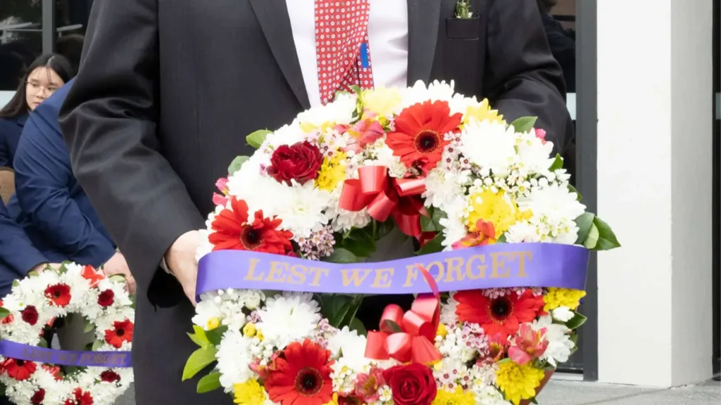 Guest holding a red and white floral wreath with a Lest We Forget ribbon at Remembrance Day 2024 at Cabravale