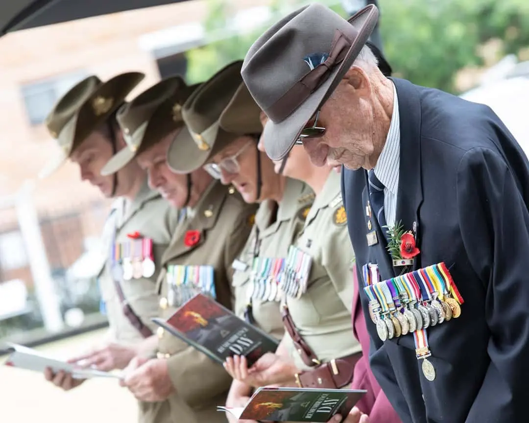 Veterans and service members wearing medals bow their heads in silence during the Remembrance Day 2024 ceremony at Cabravale Club Resort.