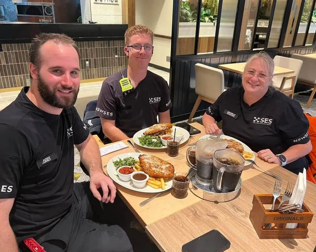 SES volunteers in uniform sit at a table enjoying hot meals and drinks at Bistro 1925 during a break from flood and storm response efforts.