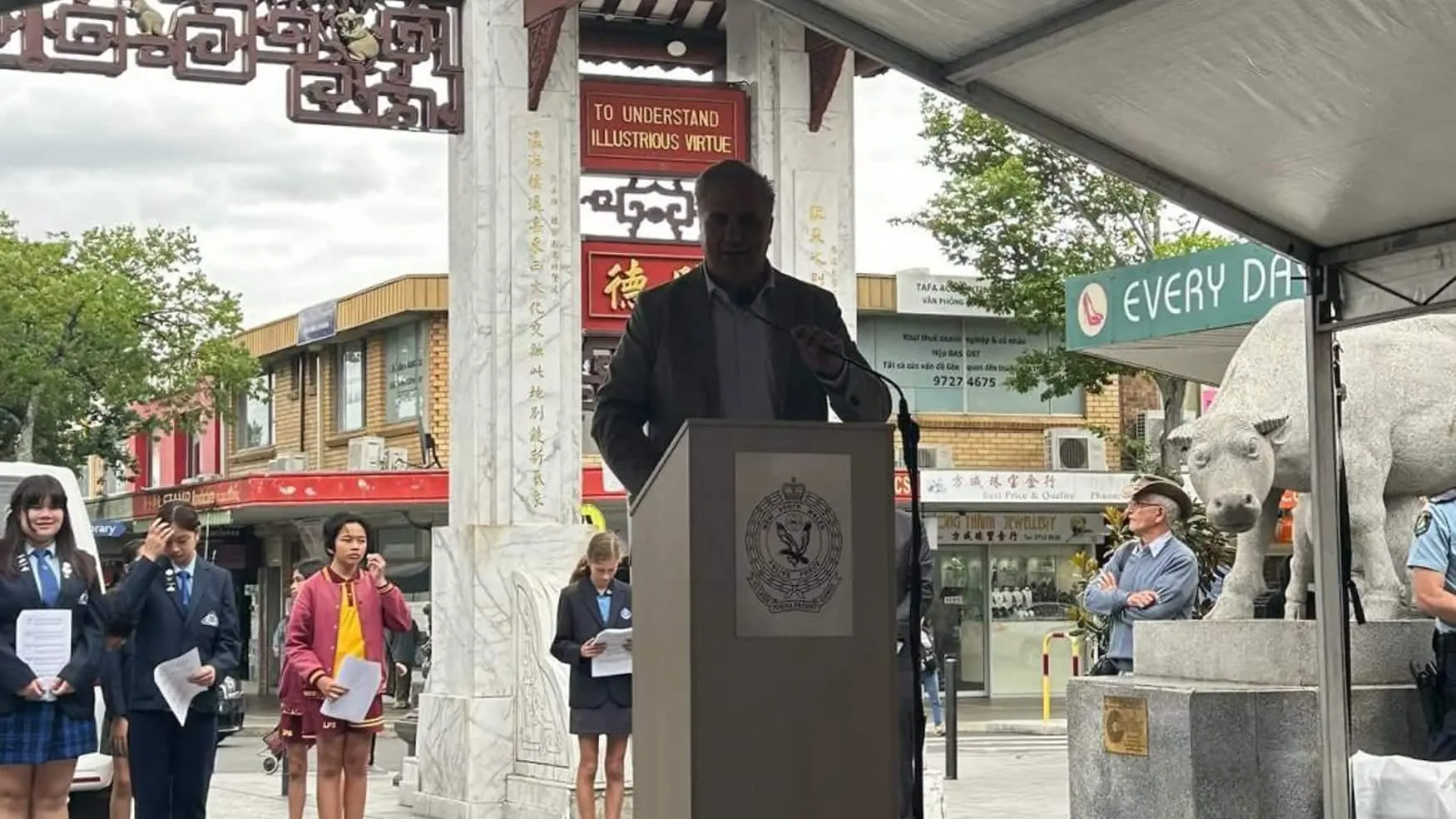 Man speaks at a podium as students and attendees gather behind at the Walk Against Domestic and Family Violence event.