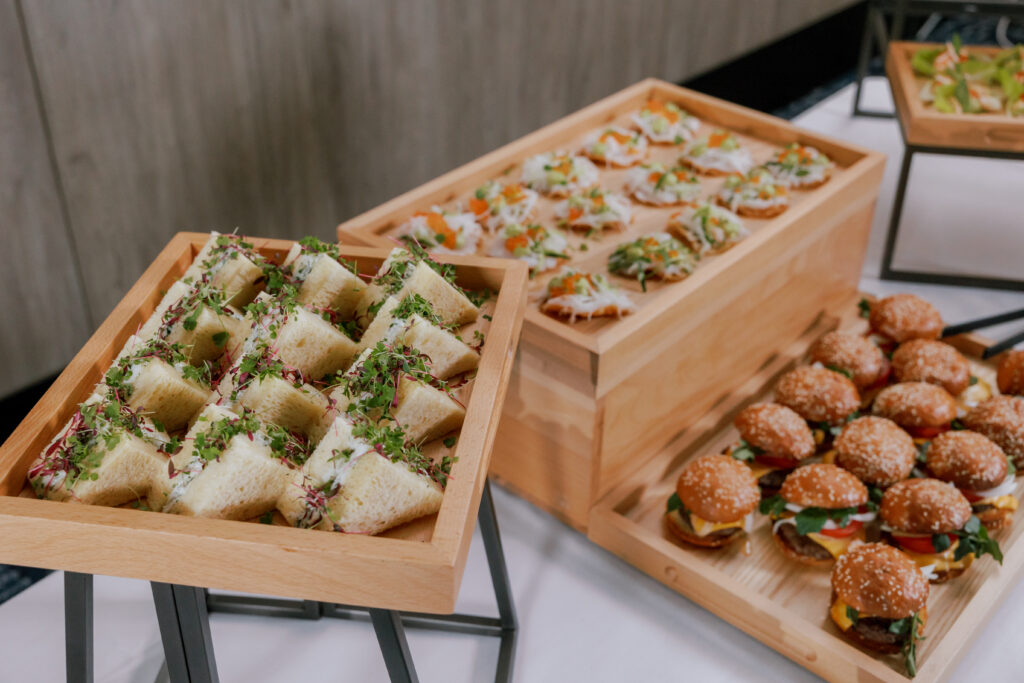 Catering display with gourmet sandwiches, canapés and mini burgers arranged on wooden trays for a conference event
