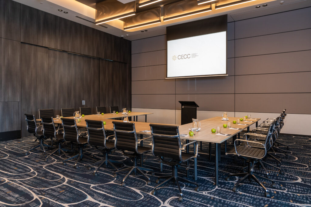 Modern conference room with U-shaped tables, AV screen displaying CECC, and green apples set for delegates
