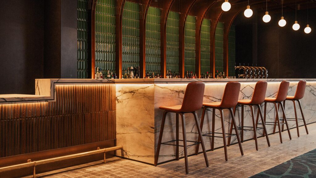 Lotus Bar with a marble-topped bar, pendant lights and high stools against green tiled walls