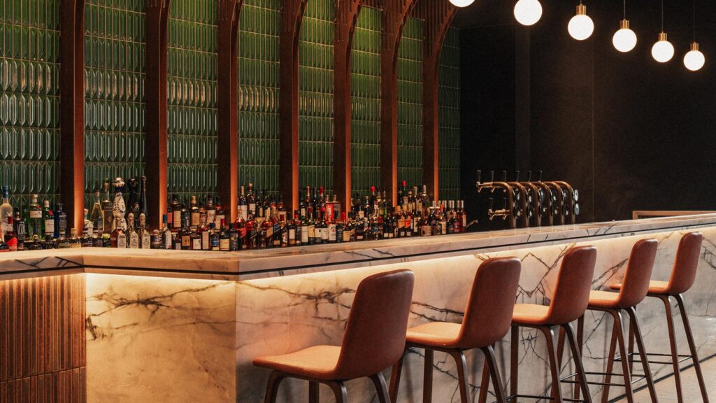 Lotus Bar counter with marble top, leather stools and a back bar of spirits under warm pendant lights