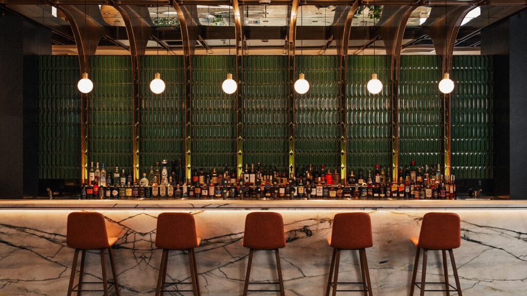 Lotus Bar cocktail counter lined with spirits, green tiled feature wall, marble bar front and warm pendant lighting