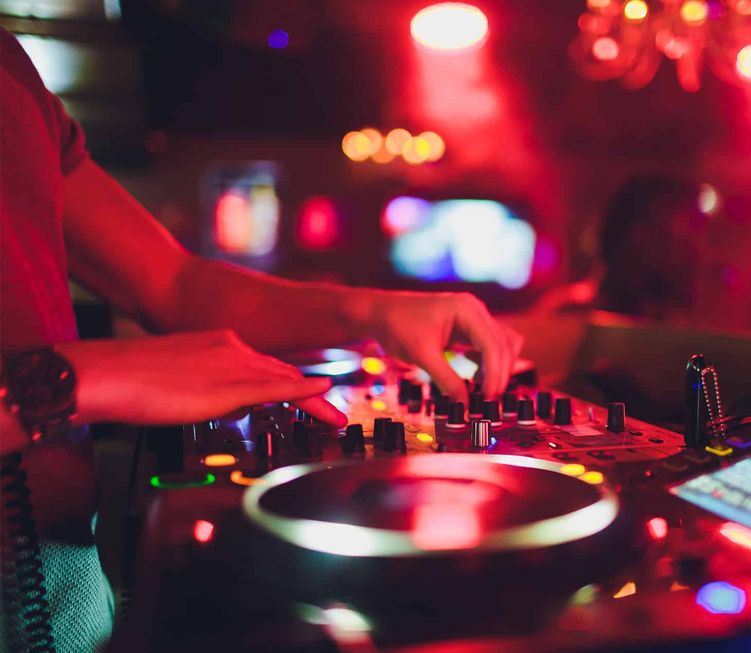 A DJ in action under deep red lights, hands on the mixer as the music drives the energy of a late-night party atmosphere in Cabravale Club Resort