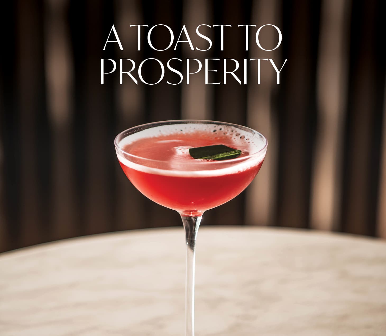 Pink cocktail in a coupe glass on marble table with elegant backdrop, featuring text “A Toast to Prosperity” for Lunar New Year celebration in Cabravale Club Resort