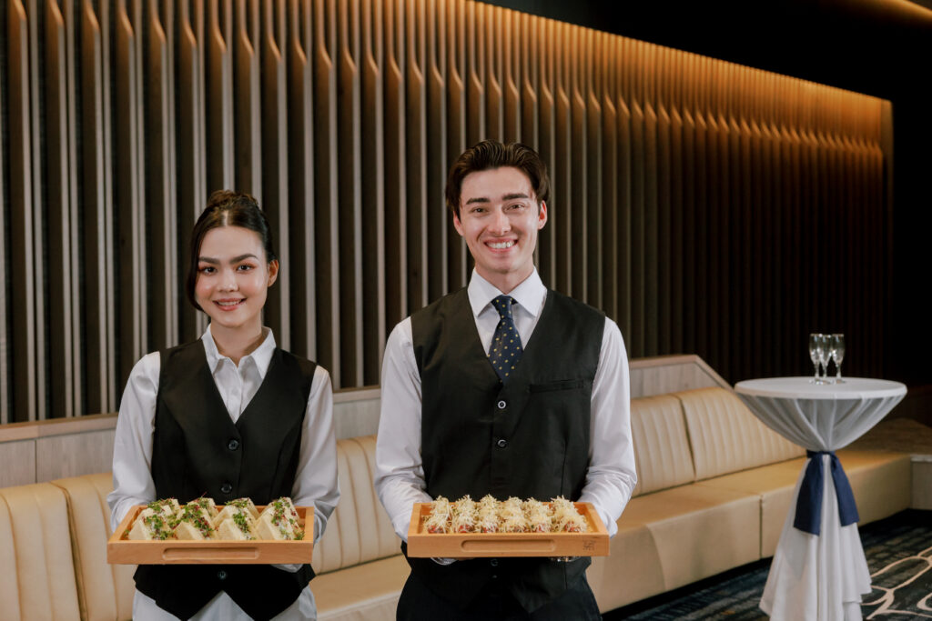Two Cabravale staff in waistcoats holding canapé platters, ready to serve at an end of year function in Western Sydney