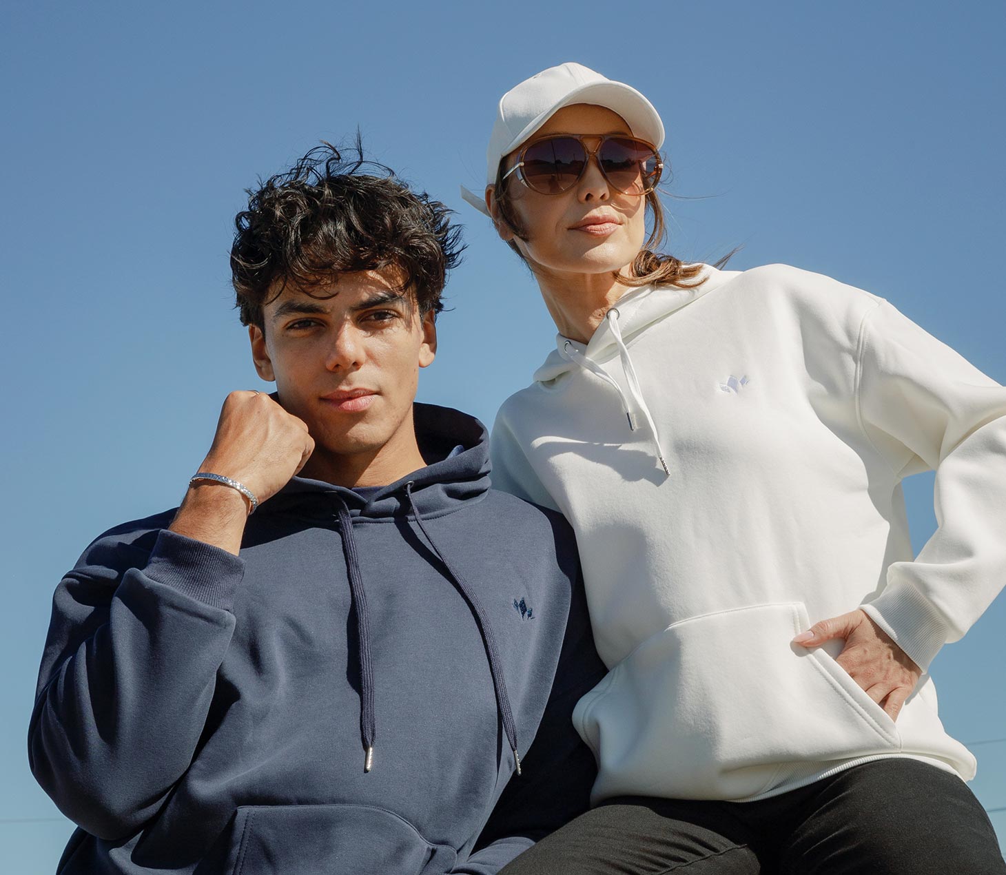 Couple wearing Cabravale Boutique navy and white hoodies against a clear blue sky