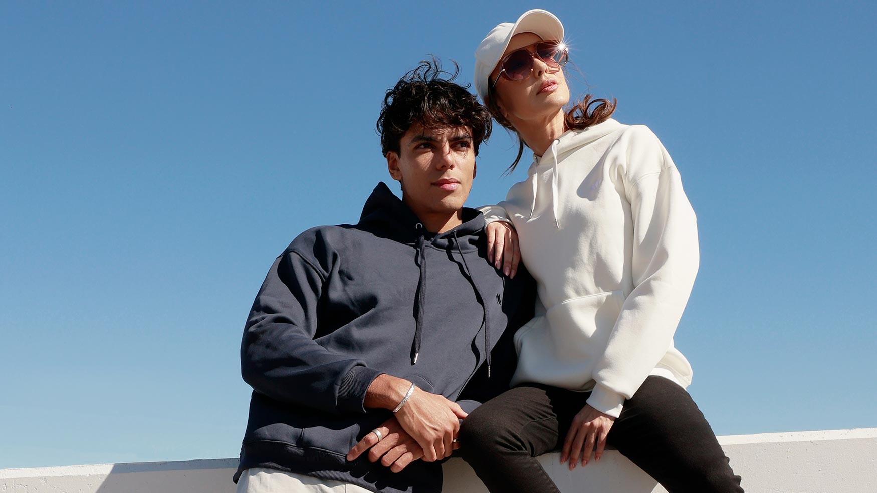 Two friends wearing Cabravale Boutique navy and white hoodies against a clear blue sky