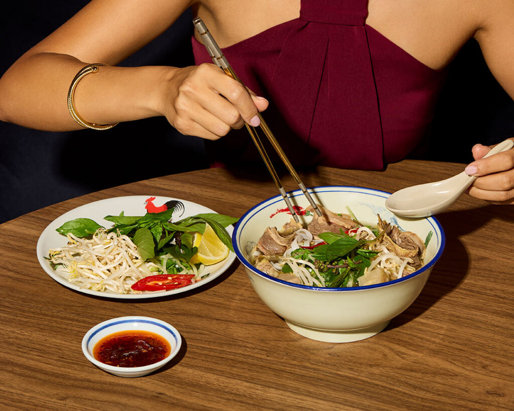 Woman eating a bowl of Vietnamese pho with fresh herbs, bean sprouts and chilli at Cabravale Club Resort