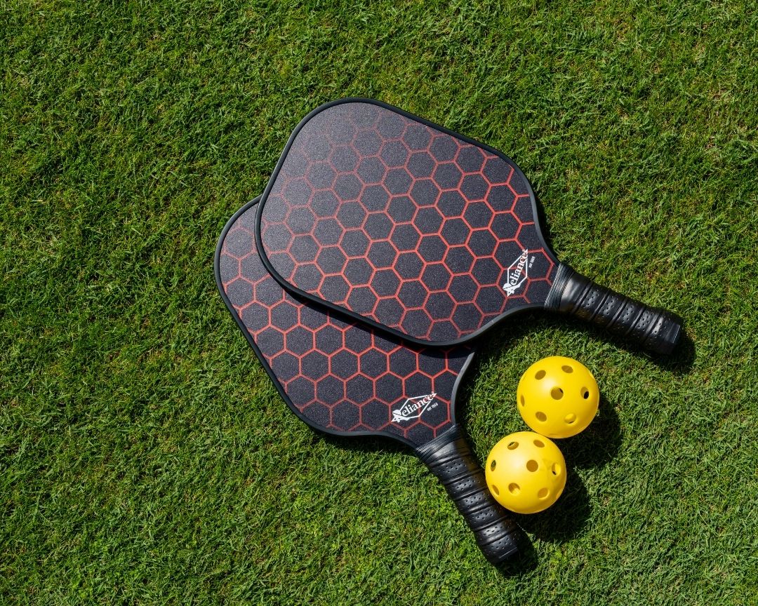 two pickleball paddles and balls on grass lawn