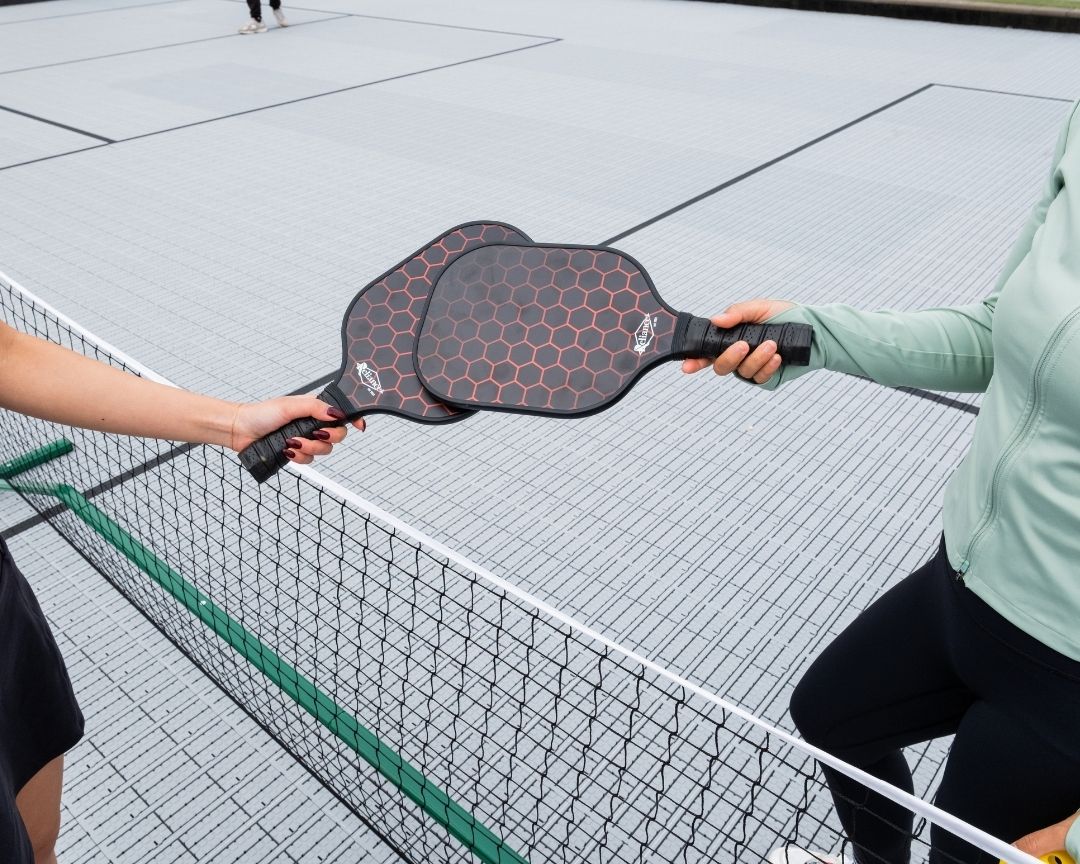 Two pickleball players touching paddles on court above net