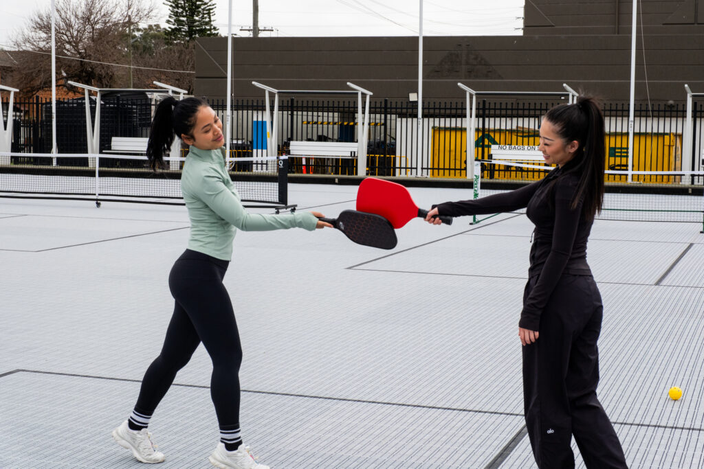 Two girls hitting paddle ball paddles on outdoor pickleball court