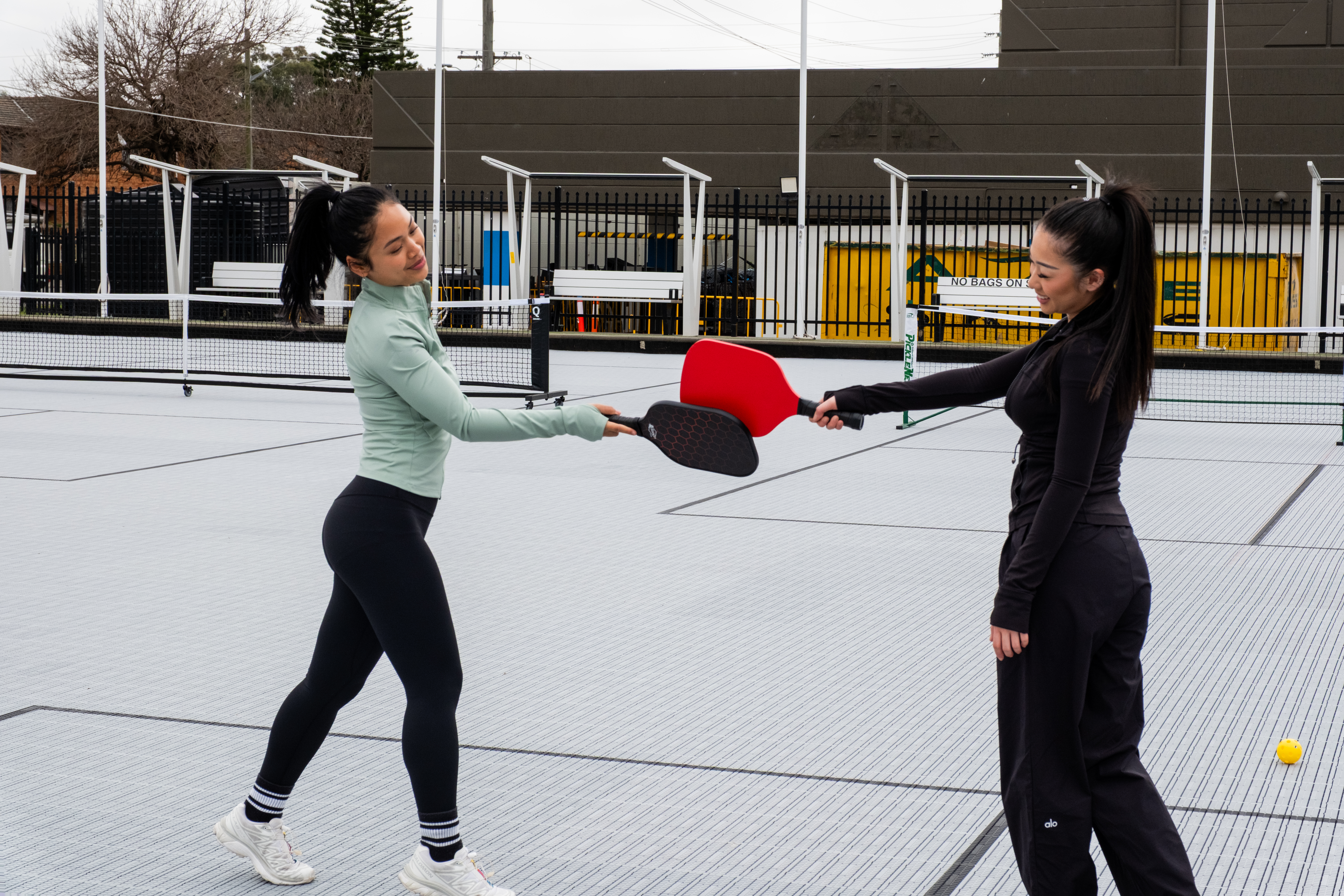 Two girls hitting paddle ball paddles on outdoor pickleball court