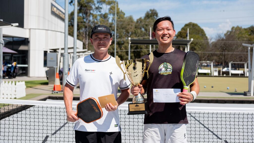 Two tournament winners holding a trophy, paddles and a prize envelope at Cabravale Pickleball in Cabramatta