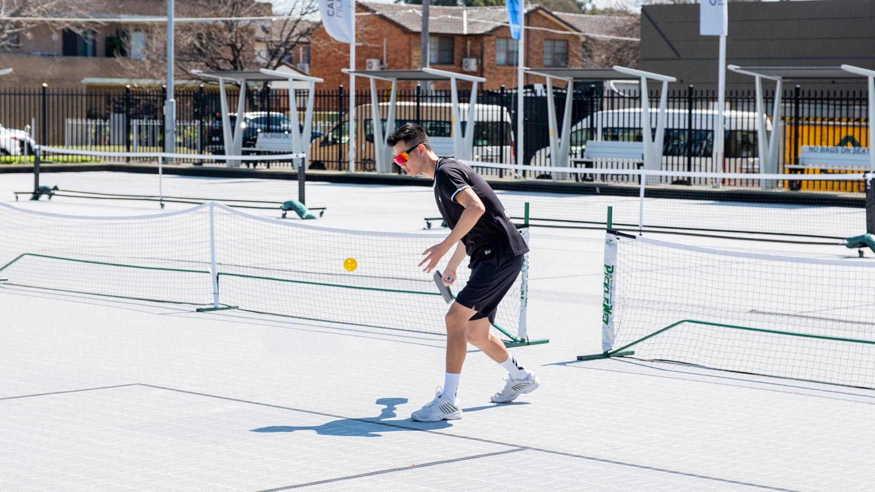 Player returning a shot on a sunny outdoor pickleball court in Cabramatta
